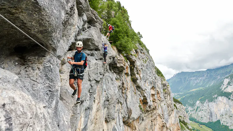 Drie mensen die een via ferrata beklimmen op een steile bergklif.